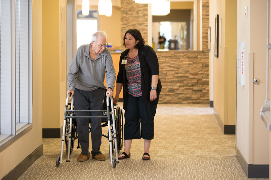 caregiver walking with elderly man down hallway