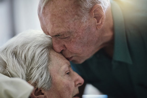 elderly man gently kissing his wife on the forehead
