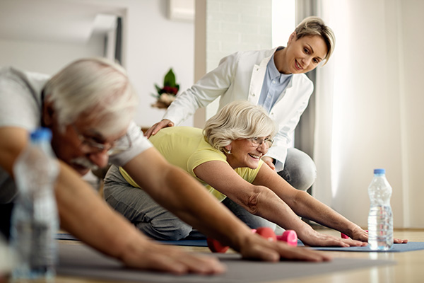 Happy mature woman and her husband stretching on the floor while exercising with physiotherapist at home.